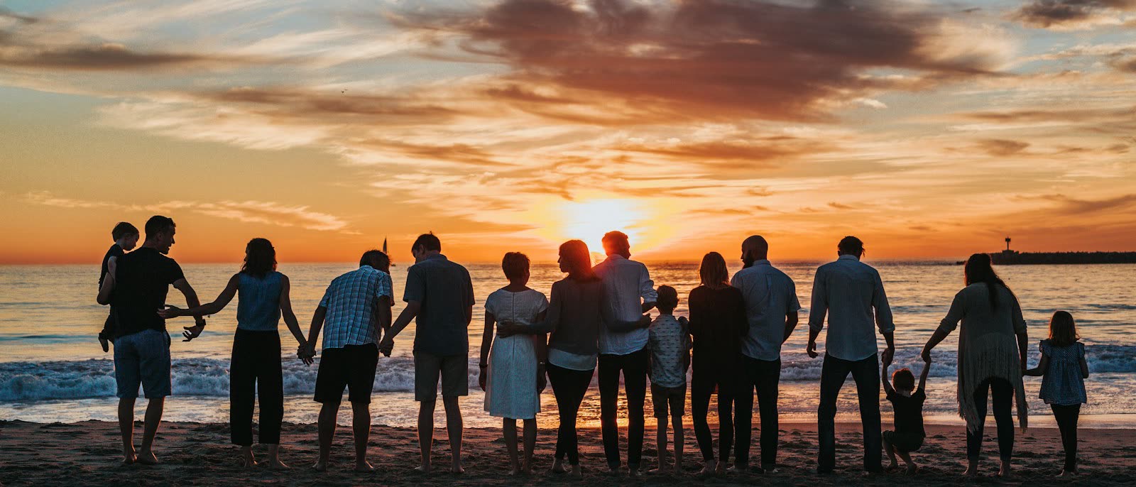 Eine große Familie steht Hand in Hand am Strand und schaut in den Sonnenuntergang.