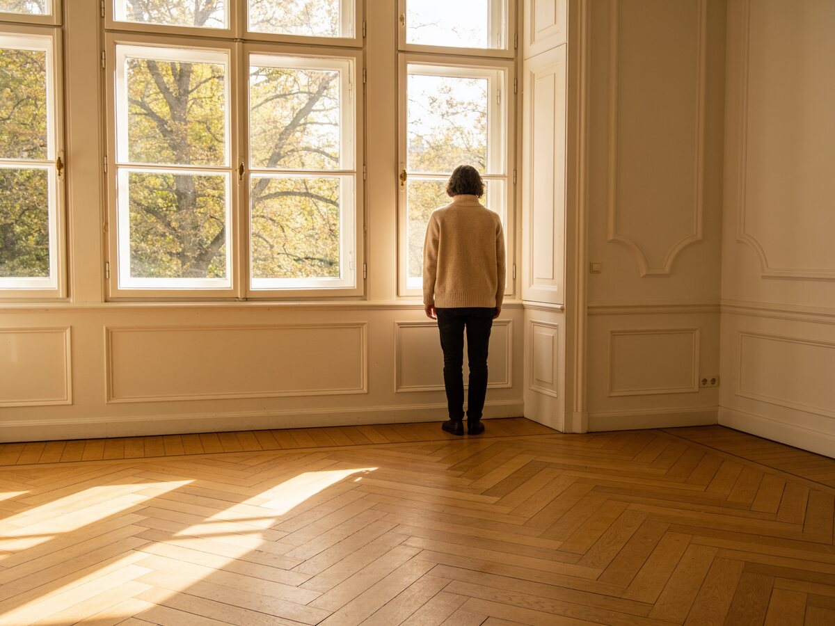 Helle, leere Altbauwohnung, eine Person schaut aus dem Fenster.
